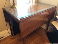 Overall front view of closed drop leaf table with glass top