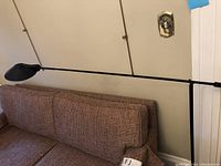 Full view of black tilting floor lamp positioned next to couch showing overall design and size.