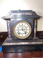 Front view of the vintage mantle clock showing clock face, gold bezel, pinkish marble accents and floral engravings on black body.