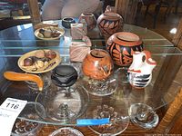 The main image showing the entire collection arranged on a glass table, capturing various pottery pieces including bowls, vases, a pitcher, and natural decor objects.