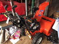Side view of Ariens Deluxe 24 AX254 snow blower showing orange housing, chute and black control handles