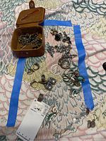 Photo showing a collection of sterling silver jewelry including rings, pins, cufflinks, and tokens in a small brown jewelry case and laid out on fabric.