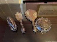 Lot arranged on dark surface: oval tray, hair brush, hand mirror, round powder box