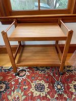Front view of wooden tea cart showing two shelves and caster wheels.