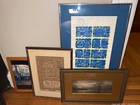 Four framed prints and photographs leaning against a wall on hardwood floor