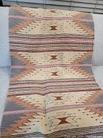Full length photo of the Navajo-style rug showing the repeating geometric pattern with earth-tone colors, draped over couch.