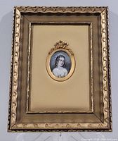 Front view of framed miniature portrait painting showing gold-tone decorative frame with oval opening and leather-like mount.