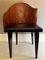 Front view of the chair showing the curved wood backrest, black leather seat, and tapered black legs.