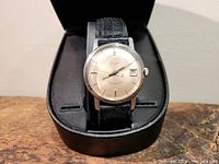 Clear image showing the full watch inside the case, emphasizing its vintage design and strap.