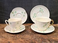 Photo of two Belleek shamrock-themed cups and saucers set side by side showing basketweave texture and hand-painted green shamrocks.