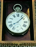 Front of antique pocket watch showing white dial with black Roman numerals and blued metal hands