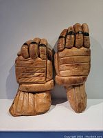Front view of pair of antique brown leather hockey gloves with padded finger sections and extended cuffs
