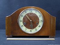 Front view of the wooden mantel clock showing dial, winding holes, and wood construction.