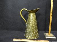 Full view of the brass water jug about 13 inches tall with textured reptile-skin style pattern.