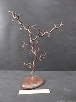 Front view of bronze jewelry display tree showing twisted branches and textured base with ruler for scale.