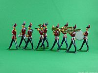 Photo of nine cast toy soldiers arranged in a marching band formation showing variety of figures with instruments and marching poses on green background.