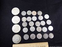 Overview of 25 Chinese dragon motif silver coins arranged on black cloth with ruler at bottom