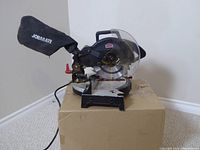 Front view of Jobmate compound mitre saw showing blade, dust bag, and baseplate angle markings.