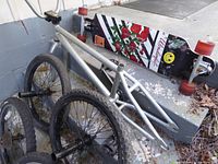 Vintage BMX bicycle frame leaning against steps with longboard and bicycle wheels nearby