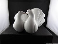 Front view of the pair of white porcelain love birds figurines with detailed bodies, red eyes, and leafy tails.