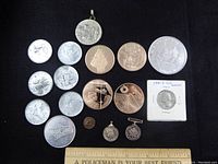 Photo of assorted Canadian Forces medals, commemorative coins, and a small token on black background with part of a ruler visible.