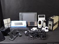 Wide view showing all items: vintage 8mm camera, security cameras, keyboards, tablet, radio, phone base stations, iPod, and cables.