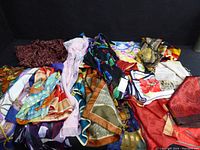 Multiple colorful scarves laid out together, showcasing various patterns and colors including a burgundy and purple velvet-like scarf.