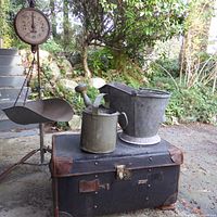 Photo showing full lot of items: hanging grain scale, galvanized watering can, galvanized coal bucket, and antique leather-trimmed chest arranged outside on ground