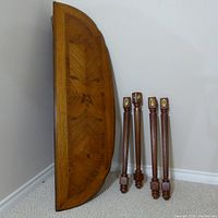 Side view of the half moon shaped ornate wooden table top and four detached carved legs with brass medallions.
