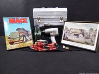 Wide shot showing all items including aluminum toolbox, pneumatic tool, Mack truck book, framed print, Coca-Cola bottle, toy truck, and collectible caps.