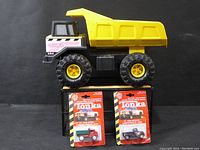 Large yellow Tonka dump truck with two smaller Tonka trucks in packaged cards on black background
