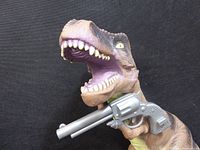 Close-up of large realistic Tyrannosaurus rex toy figure holding a plastic gun