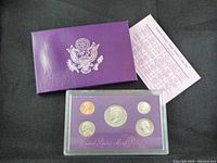 Purple folder with the Great Seal embossed and coins in protective plastic case displayed on purple card.