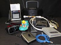 Photo showing entire lot including vintage Sony Watchman FD-230 portable TV, Sony boombox, Nintendo Game Boy game case, electronic cables, retro joystick toy, and other miscellaneous electronic devices and accessories.