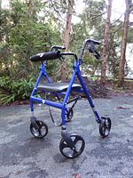 Blue wheeled walker with seat and backrest on an outdoor surface near trees.