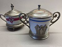 Front and side view showing two vintage sugar bowls with ceramic bodies and metal framing and lids, highlighting the decorative metalwork and ceramic patterns.