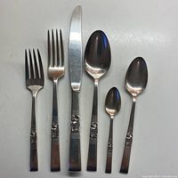 Flatware utensils arranged to show different types: forks, knife, spoons of varying sizes all with the floral orchid design on handles.