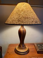 Full view of the hand turned wooden lamp with speckled cream shade on a wood surface under warm lighting.