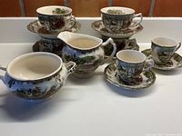 Full set of tea and cappuccino cups with saucers, creamer, and sugar bowl all featuring winter village designs.