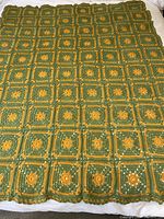 Full view of the crocheted blanket laid flat, showing all crocheted squares in olive green and amber with scalloped edges