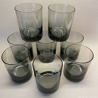 Eight smoky grey lowball glasses arranged with two glasses elevated and the others grouped underneath, showing the overall shape and color.