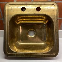 Top view of solid brass sink showing two faucet holes and central drain hole, tarnished surface with some patina and spots.