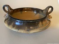 Angled front view of the brown and caramel glazed pottery bowl showing the handles and overall shape.