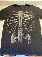 Front view of black T-shirt featuring a white graphic of a guitar neck incorporated as a spine with ribs formed from microphone cables and a microphone.