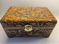 Front view of the carved wooden box showing the brass closure and detailed dragon and cloud design.