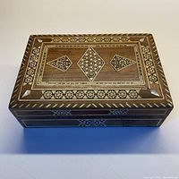 Top view of vintage wooden box showing detailed inlaid geometric and floral patterns with mother of pearl corner accents.