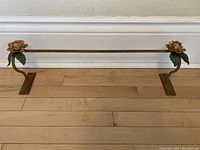 Full view of the vintage wrought iron towel rack laid horizontally showing flower details at each end and rust finish.