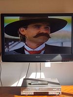 Sony TV screen displaying Western movie scene, Samsung DVD/VCR player below it on table.