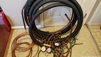 Photo showing several coiled copper tubing lines and black insulated hoses on floor along wall.