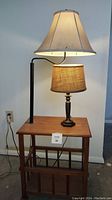 Wooden table with built-in black metal lamp arm and large beige fabric lampshade, small dresser lamp on top